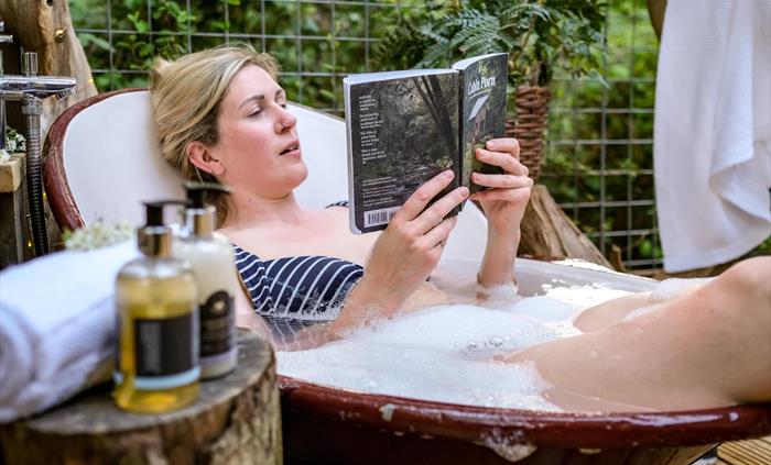 Woman takes outdoor bath in woodland.  Glamping Holidays in Hay-on-Wye